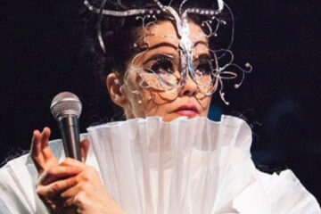 Björk segurando um microfone e usando uma máscara artística detalhada, durante apresentação ao vivo.
