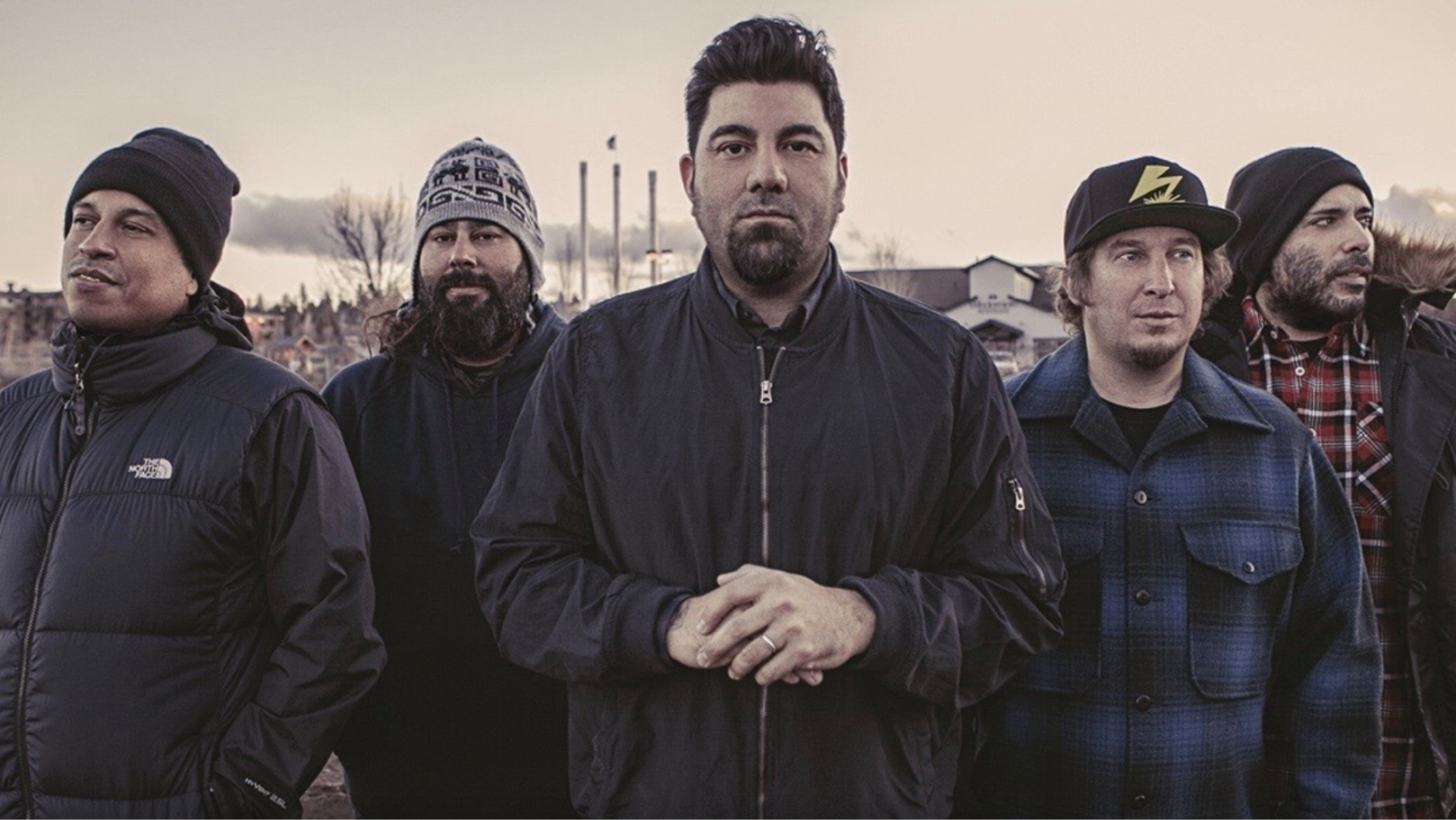 Foto da banda Deftones reunida ao ar livre, com Chino Moreno ao centro e os demais integrantes posando de casacos em clima frio.