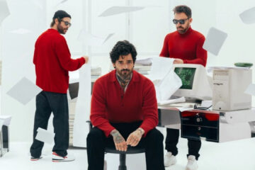 Integrantes da Fresno em estúdio branco, vestindo roupas vermelhas, com papéis voando e computador antigo exibindo “Carta de Adeus” na tela.