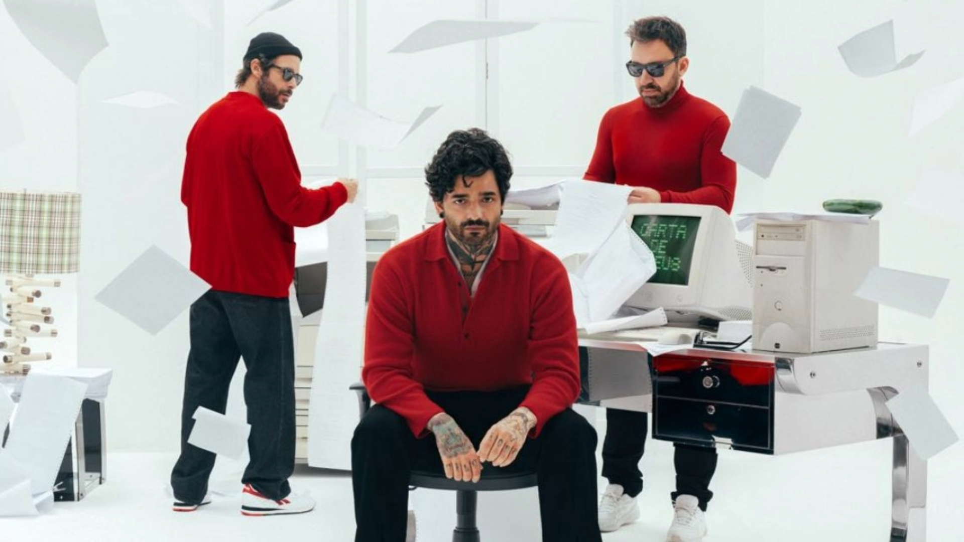 Integrantes da Fresno em estúdio branco, vestindo roupas vermelhas, com papéis voando e computador antigo exibindo “Carta de Adeus” na tela.