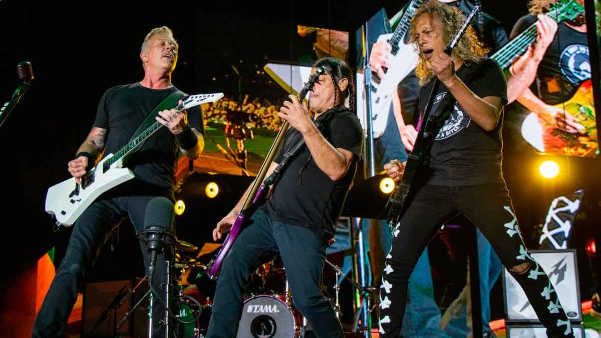 James Hetfield, Robert Trujillo e Kirk Hammett tocando ao vivo durante show do Metallica.
