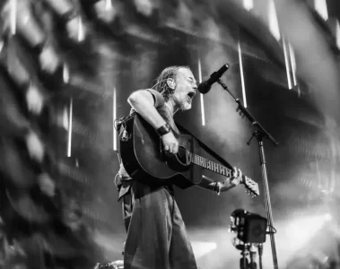 Thom Yorke tocando violão e cantando em um show do Radiohead, com iluminação intensa no palco. Foto: @twoshortdays.