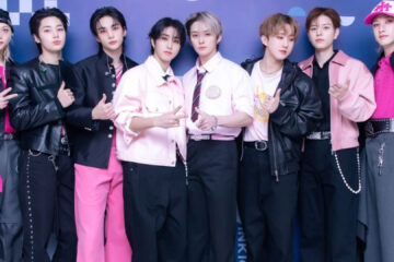 Foto do grupo Stray Kids posando juntos em evento, usando roupas em tons de preto e rosa — X/Reprodução.