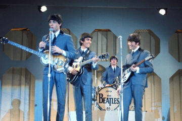 Os Beatles se apresentando ao vivo nos anos 60, com Paul McCartney, George Harrison, John Lennon e Ringo Starr no palco com seus instrumentos.
