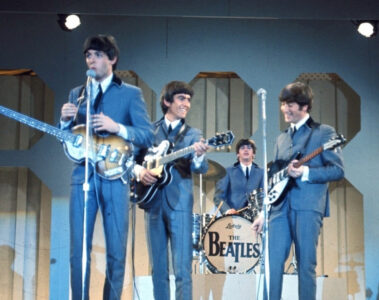 Os Beatles se apresentando ao vivo nos anos 60, com Paul McCartney, George Harrison, John Lennon e Ringo Starr no palco com seus instrumentos.
