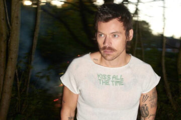 Harry Styles em imagem promocional usando camiseta com o nome do novo álbum Kiss All the Time
