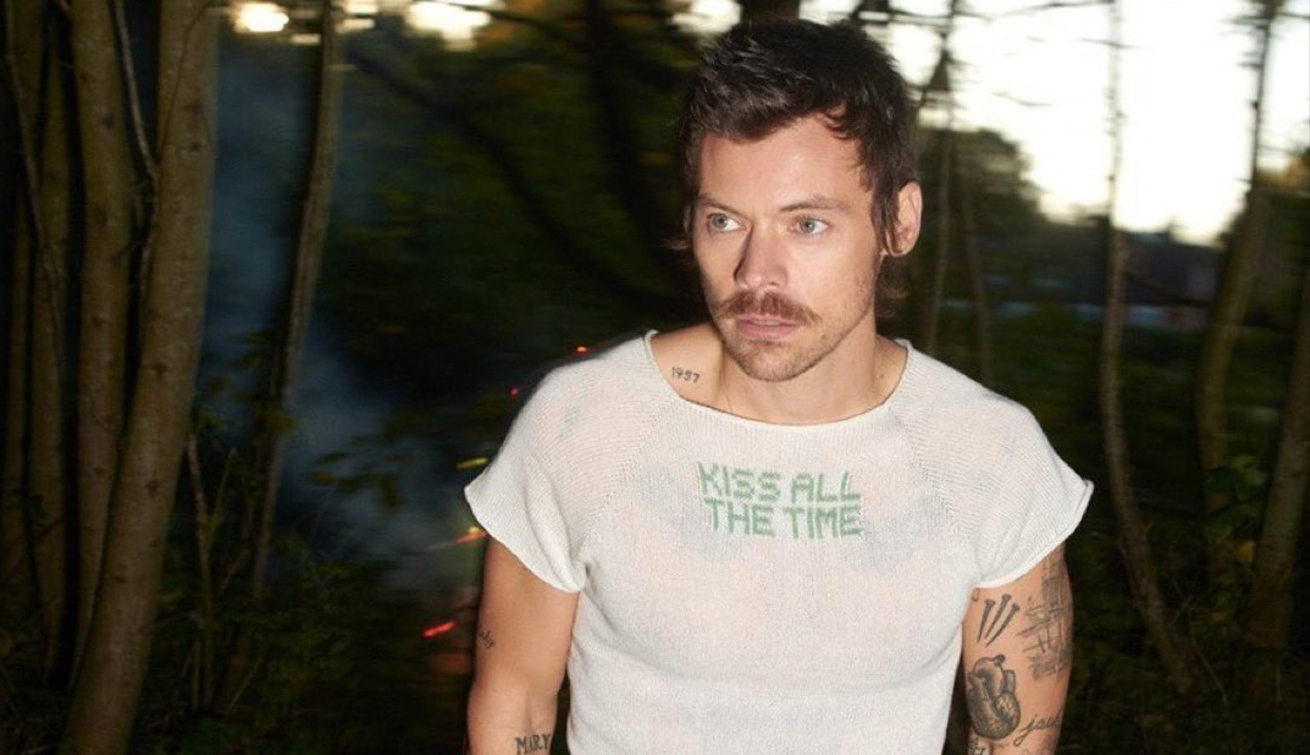Harry Styles em imagem promocional usando camiseta com o nome do novo álbum Kiss All the Time