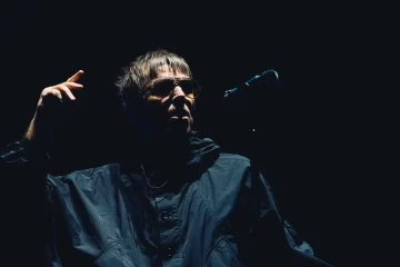 Liam Gallagher durante apresentação ao vivo do Oasis, sob iluminação baixa no palco.