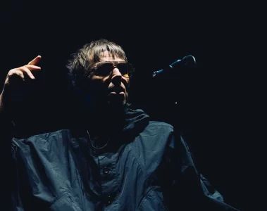 Liam Gallagher durante apresentação ao vivo do Oasis, sob iluminação baixa no palco.