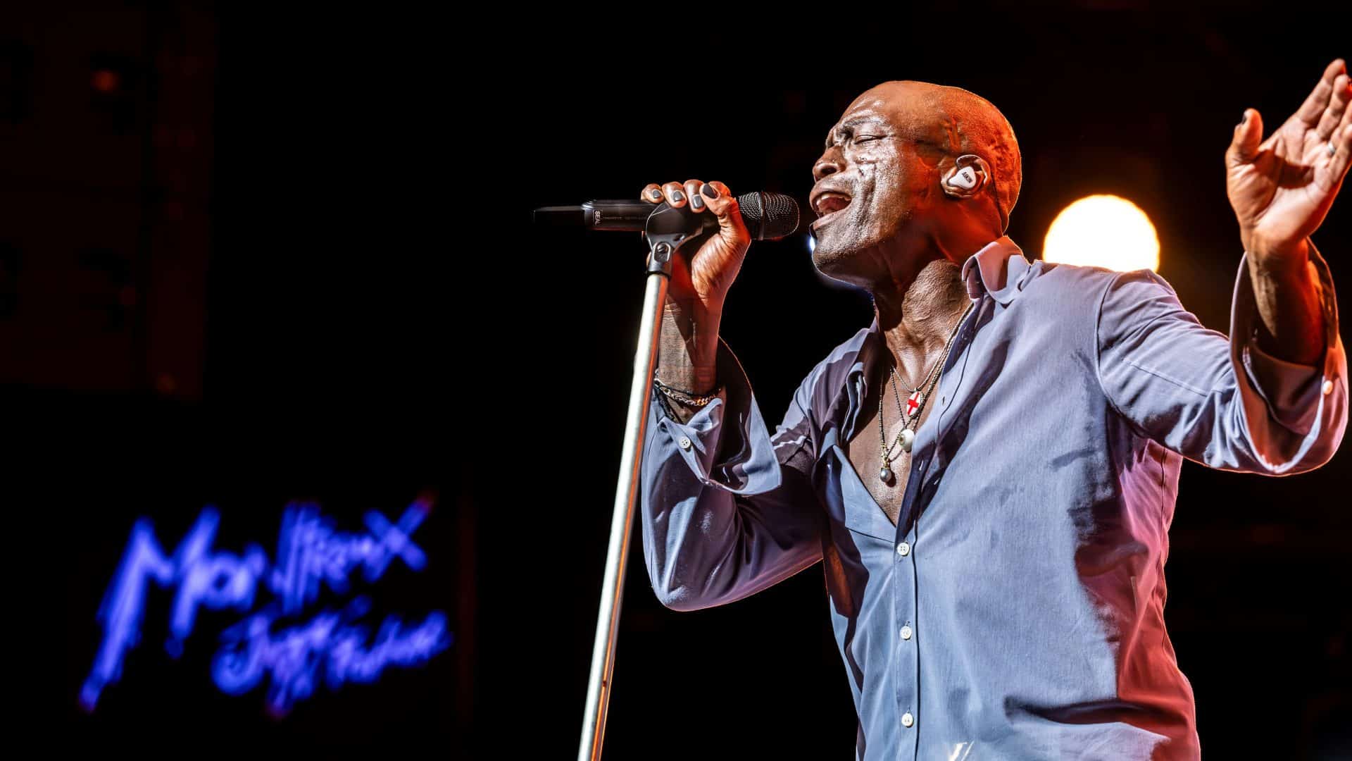 Seal cantando ao vivo em show com microfone e iluminação de palco durante turnê internacional