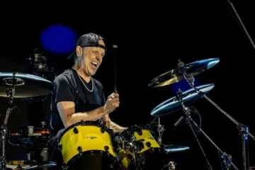 Lars Ulrich tocando bateria durante show do Metallica com expressão intensa
