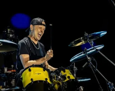 Lars Ulrich tocando bateria durante show do Metallica com expressão intensa