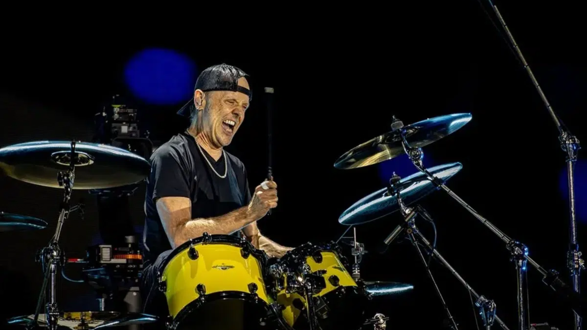 Lars Ulrich tocando bateria durante show do Metallica com expressão intensa