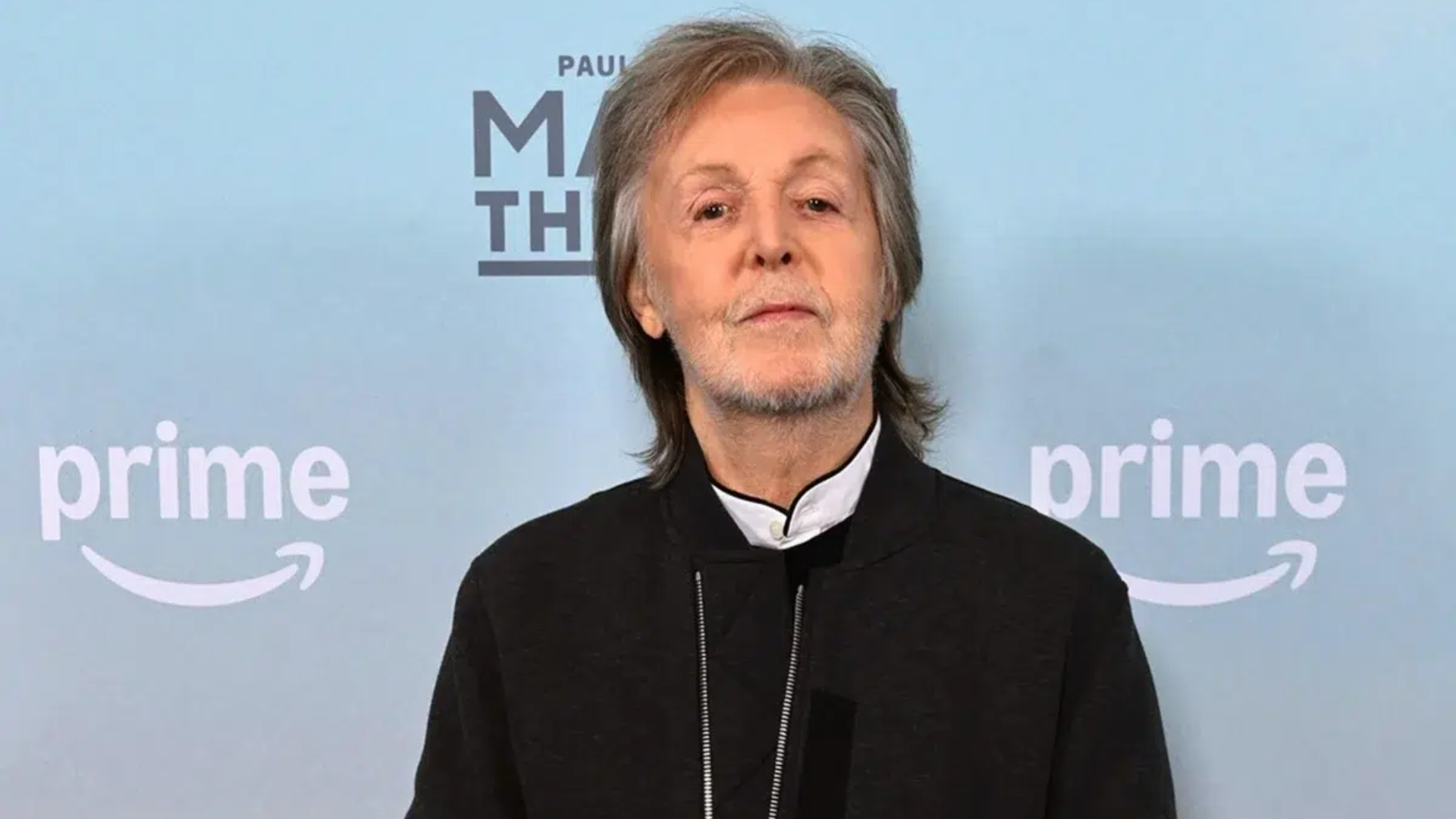 Paul McCartney em evento promocional com fundo azul e logo do Prime Video