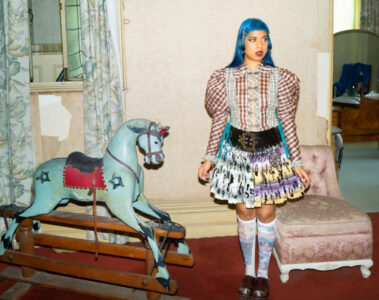 Ecca Vandal em cenário vintage com vestido colorido durante ensaio promocional