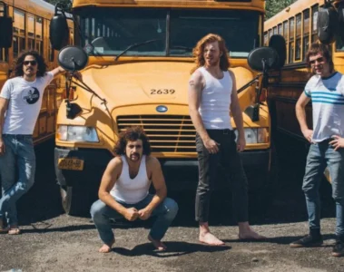 banda Sticky Fingers posando em frente a ônibus amarelos durante divulgação de turnê