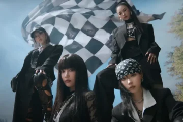 Integrantes do aespa em cena do clipe Rich Man com figurino preto e bandeira ao fundo