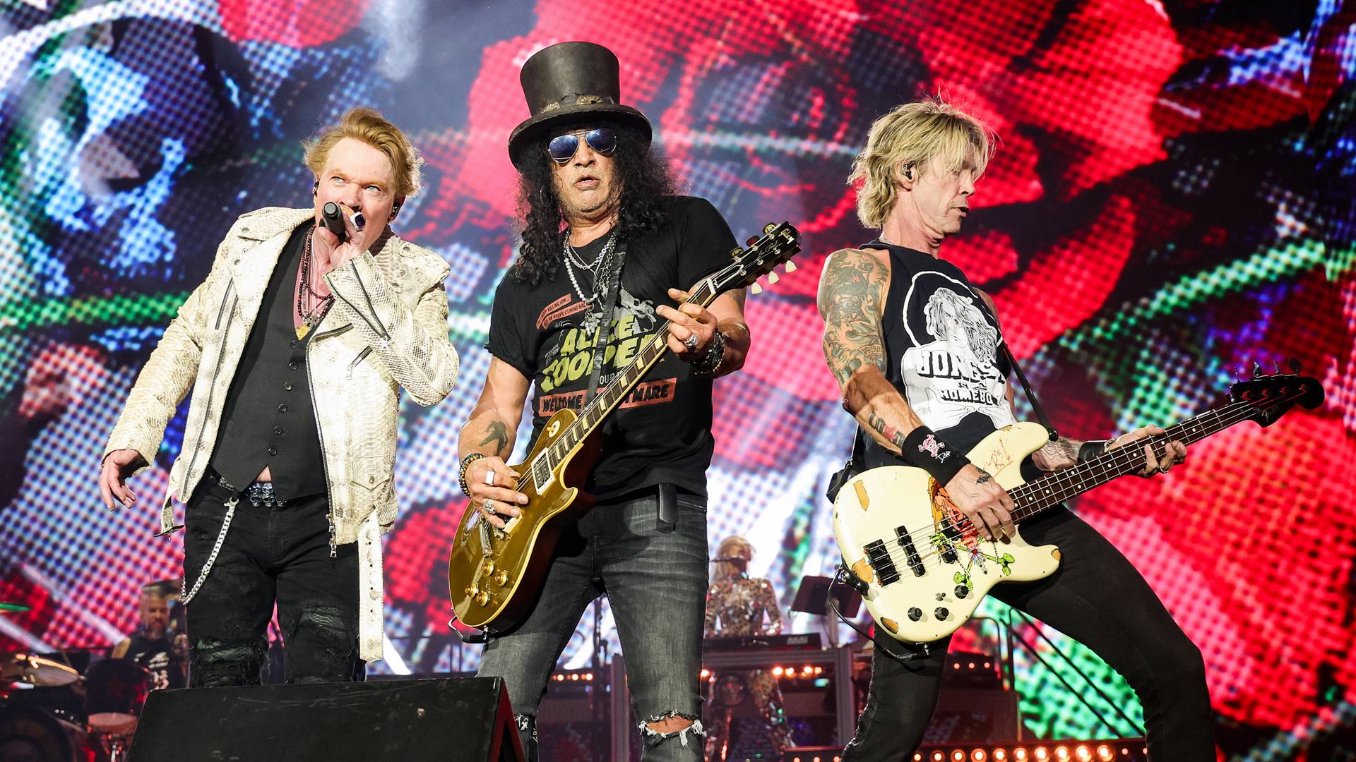 Axl Rose, Slash e Duff McKagan em show do Guns N’ Roses no palco com iluminação colorida
