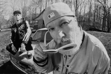 Machine Gun Kelly e Fred Durst em cena de videoclipe em preto e branco para a música “FIX UR FACE”, com estética crua e visual urbano.