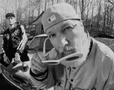 Machine Gun Kelly e Fred Durst em cena de videoclipe em preto e branco para a música “FIX UR FACE”, com estética crua e visual urbano.