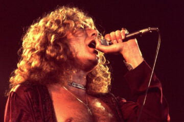 Robert Plant cantando ao vivo nos anos 70, durante apresentação do Led Zeppelin, segurando o microfone com intensidade.