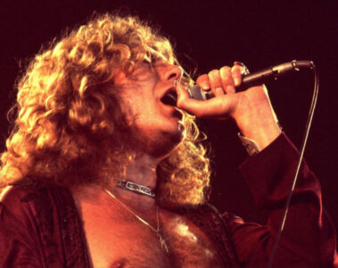 Robert Plant cantando ao vivo nos anos 70, durante apresentação do Led Zeppelin, segurando o microfone com intensidade.