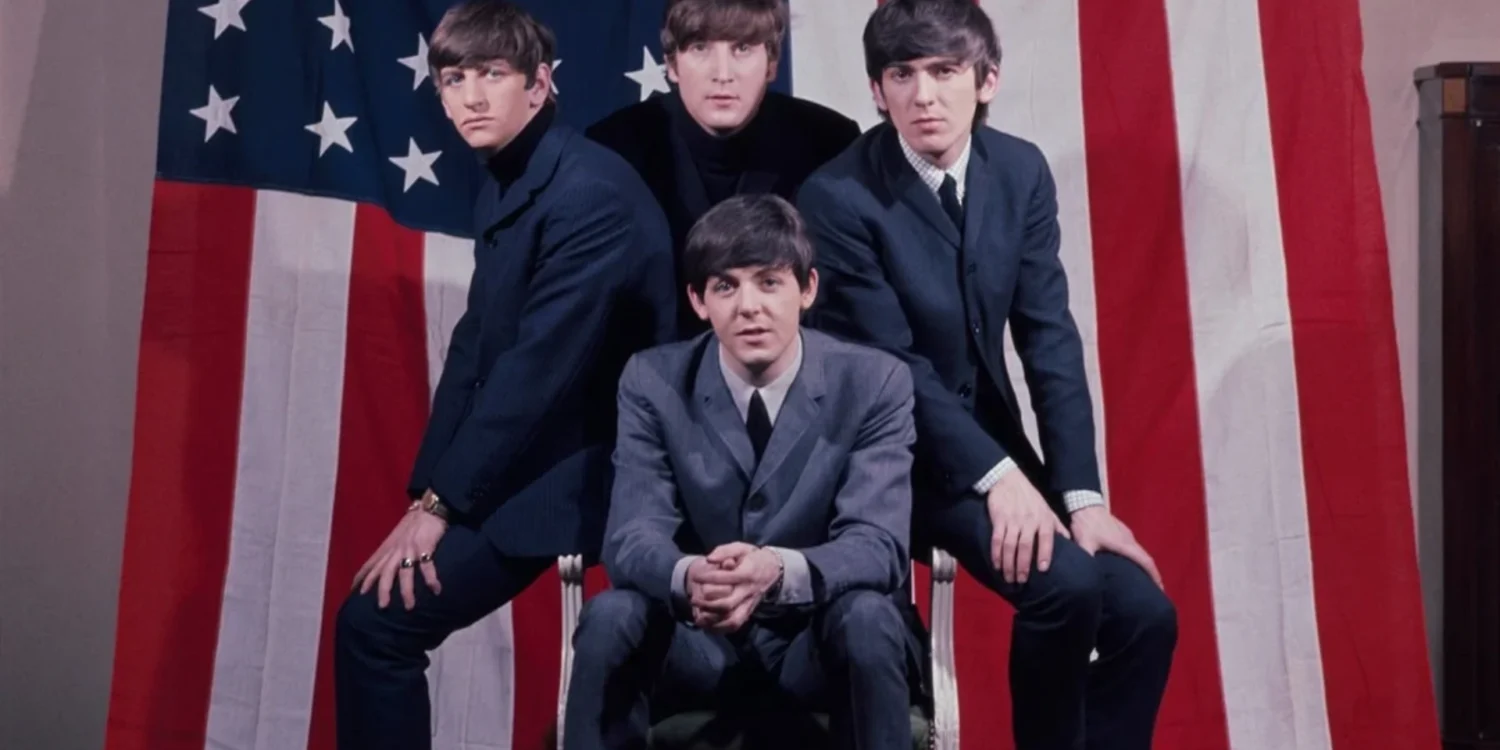 Os Beatles posam em frente à bandeira dos Estados Unidos durante a fase inicial da Beatlemania em 1964