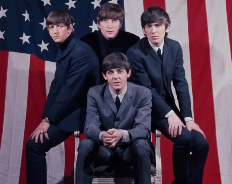 Os Beatles posam em frente à bandeira dos Estados Unidos durante a fase inicial da Beatlemania em 1964