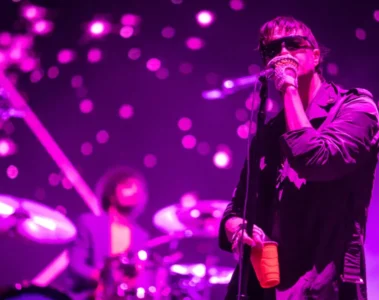 Julian Casablancas cantando ao vivo com o The Strokes sob luzes roxas, durante apresentação com a banda no palco.