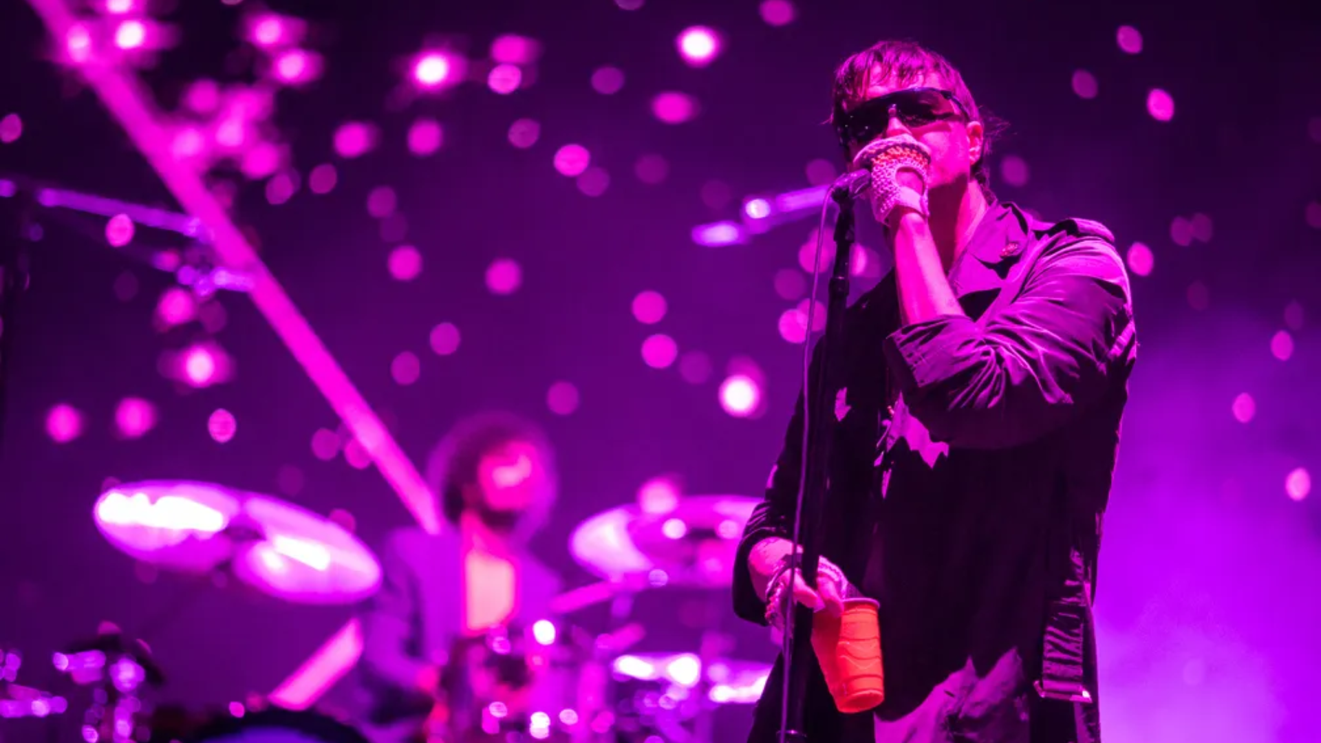 Julian Casablancas cantando ao vivo com o The Strokes sob luzes roxas, durante apresentação com a banda no palco.
