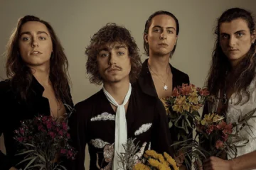 Integrantes do Greta Van Fleet posando juntos em ensaio fotográfico com flores