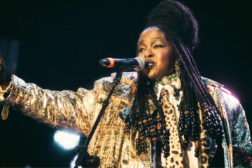 Lauryn Hill cantando durante apresentação ao vivo com figurino dourado