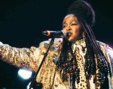 Lauryn Hill cantando durante apresentação ao vivo com figurino dourado