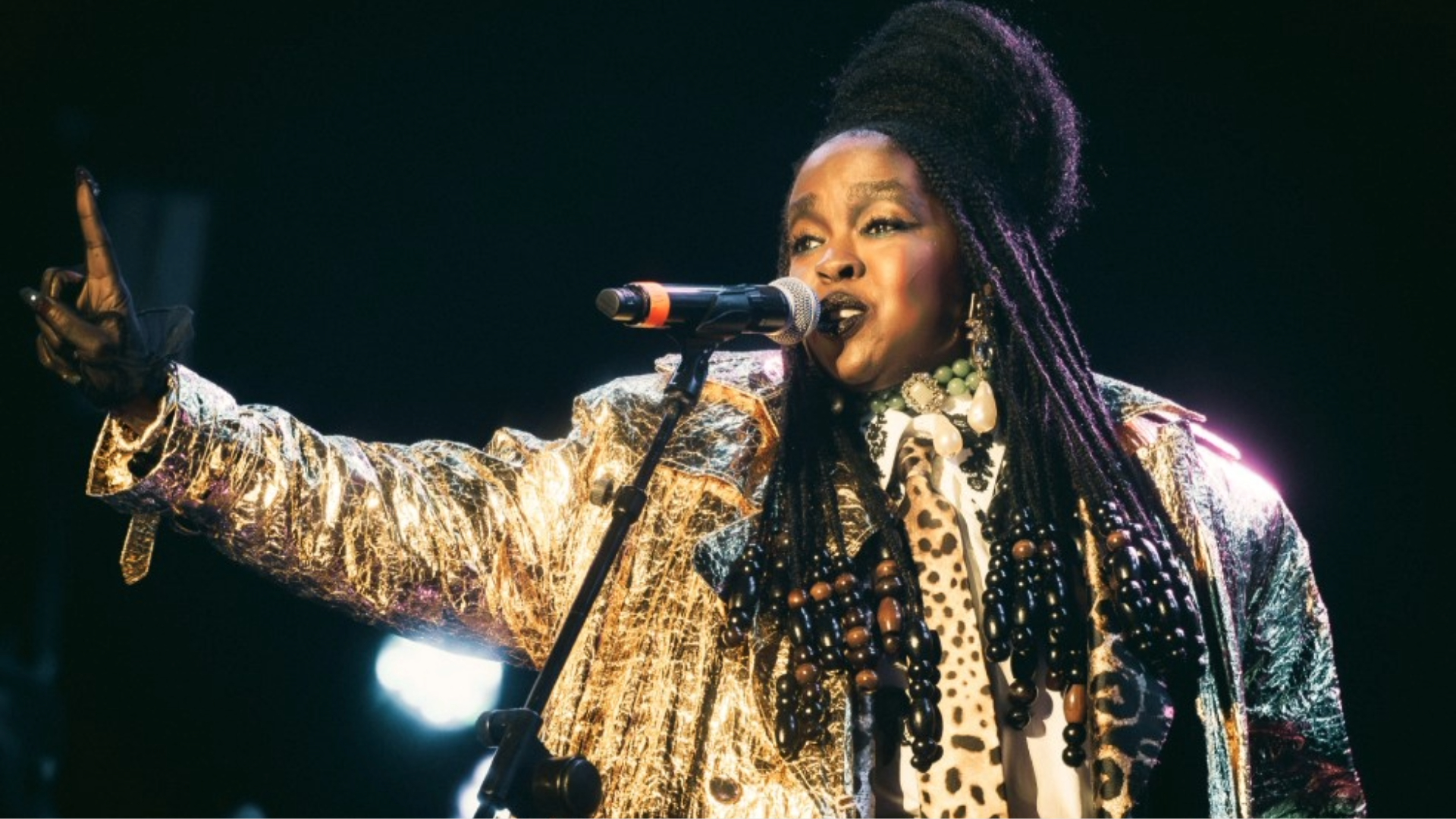 Lauryn Hill cantando durante apresentação ao vivo com figurino dourado