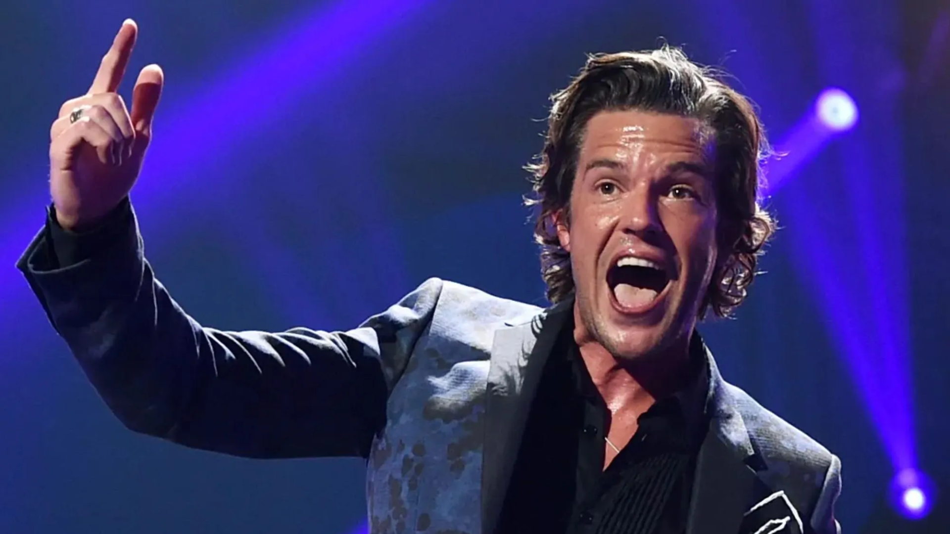 Brandon Flowers cantando durante show do The Killers com iluminação de palco