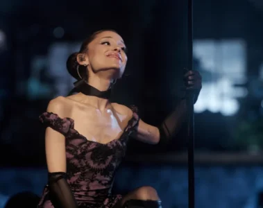 Ariana Grande se apresenta durante a estreia da Eternal Sunshine Tour, usando vestido preto e rosa enquanto interage com o público no palco.