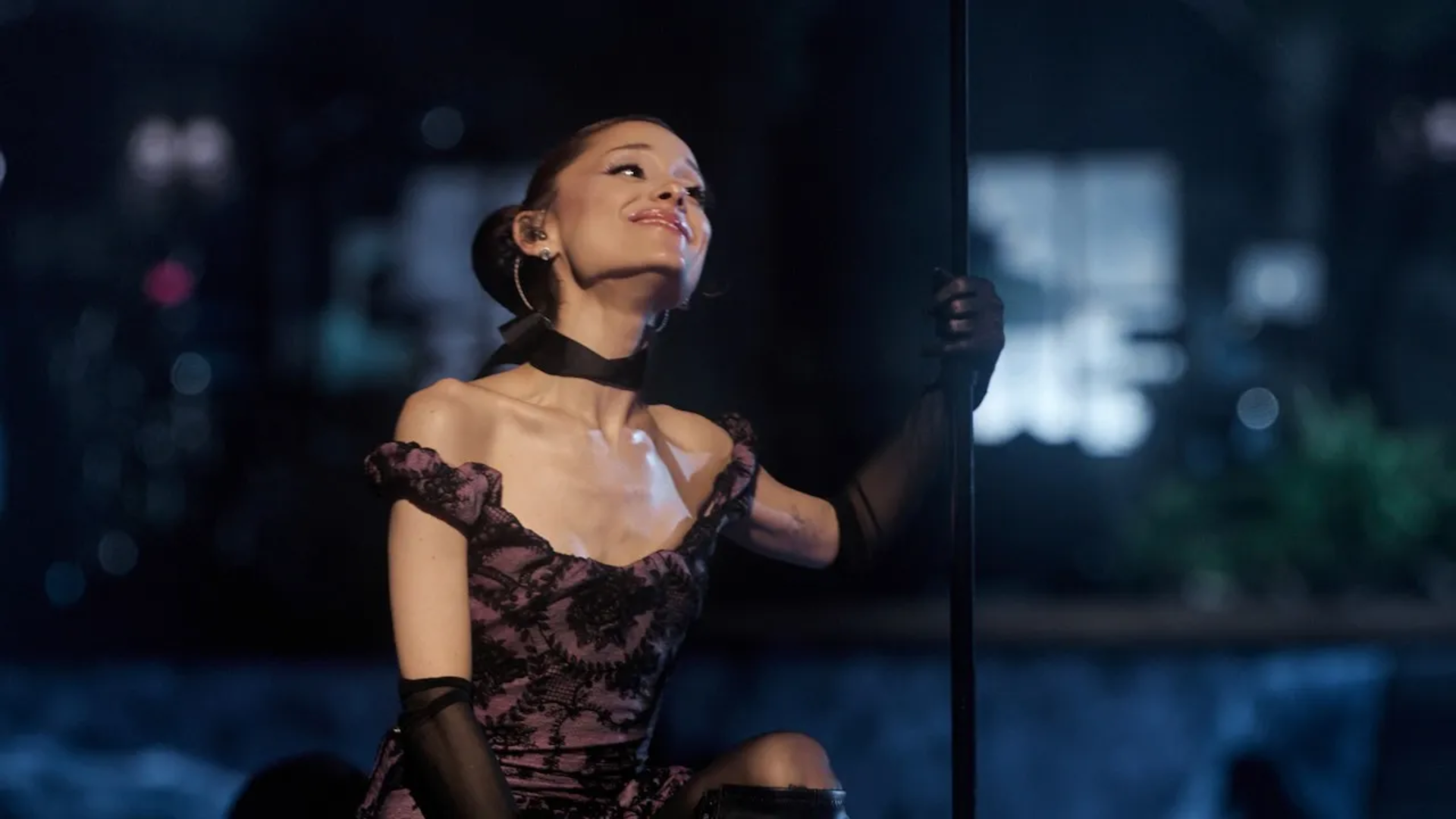 Ariana Grande se apresenta durante a estreia da Eternal Sunshine Tour, usando vestido preto e rosa enquanto interage com o público no palco.