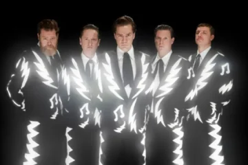 Integrantes do The Hives usando ternos preto e branco em foto promocional da banda sueca de garage rock.