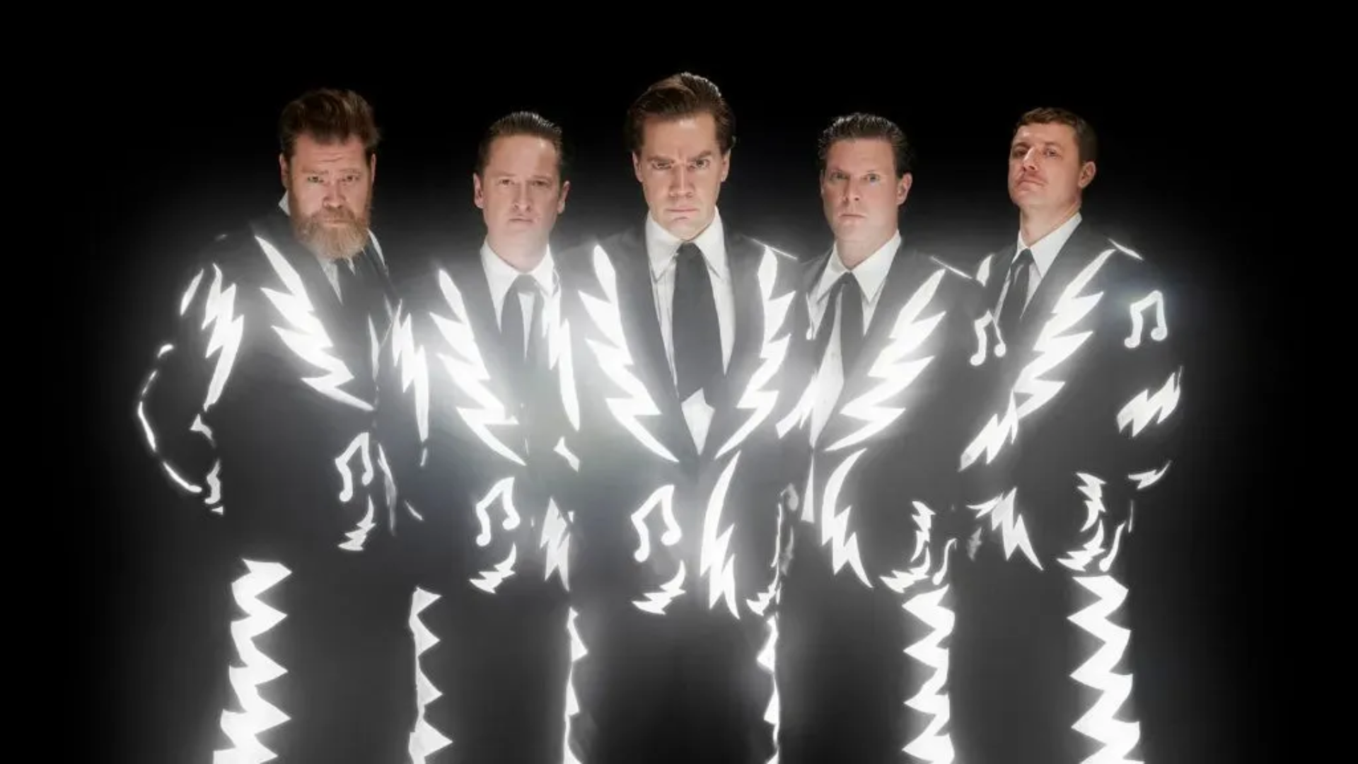 Integrantes do The Hives usando ternos preto e branco em foto promocional da banda sueca de garage rock.