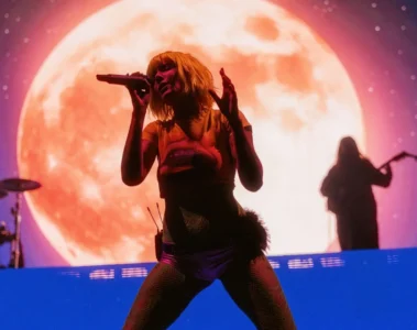 Halsey canta no palco durante uma apresentação com uma grande lua iluminada ao fundo.