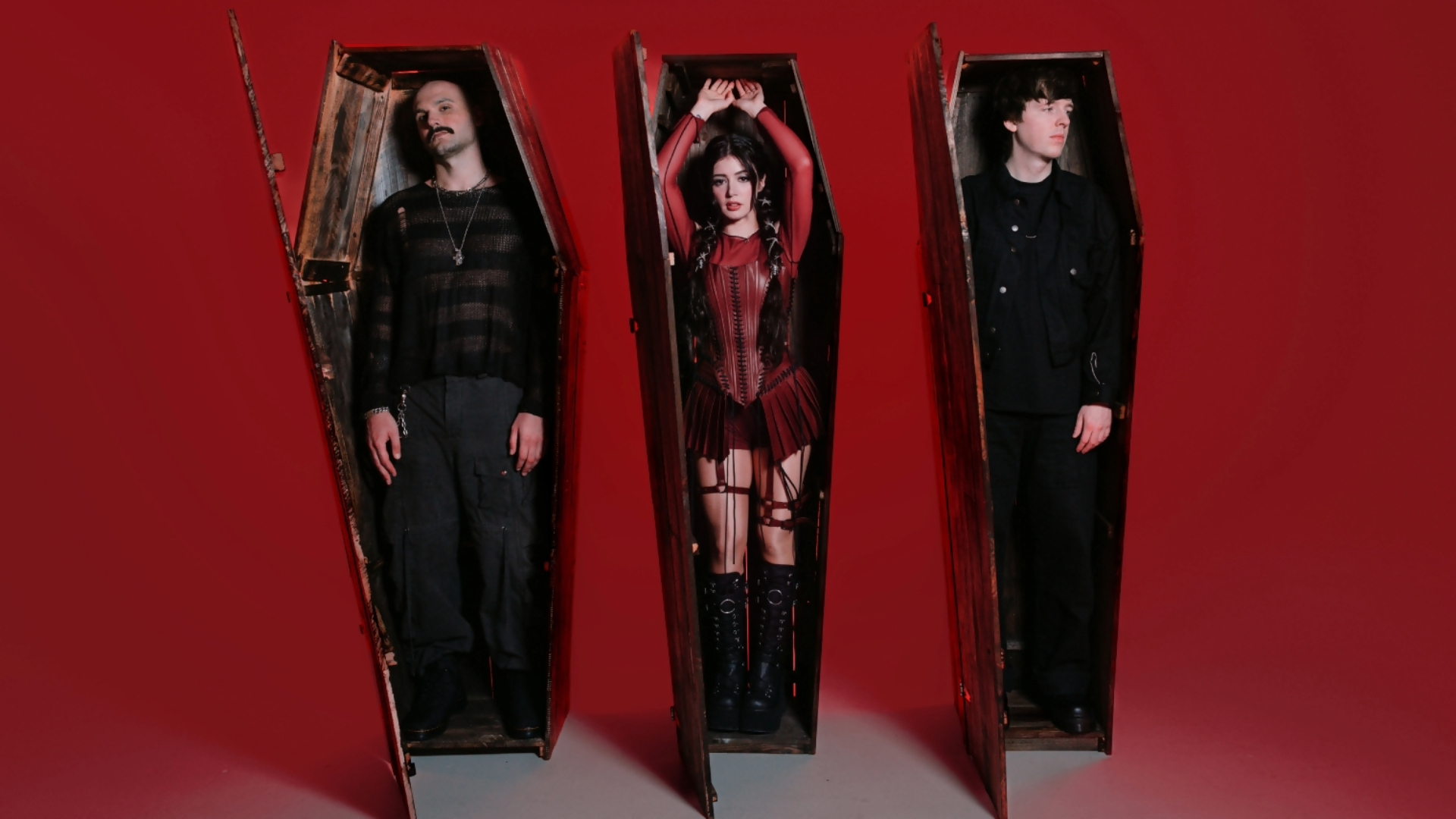 Integrantes do Against The Current, com Chrissy Costanza ao centro, posam dentro de caixões de madeira diante de um fundo vermelho.