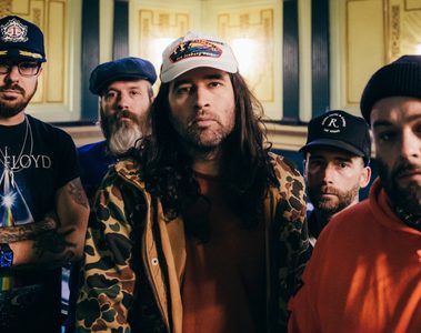 Os cinco integrantes do Alexisonfire posam juntos em fotografia promocional, usando bonés, gorros e roupas casuais, em um ambiente interno.