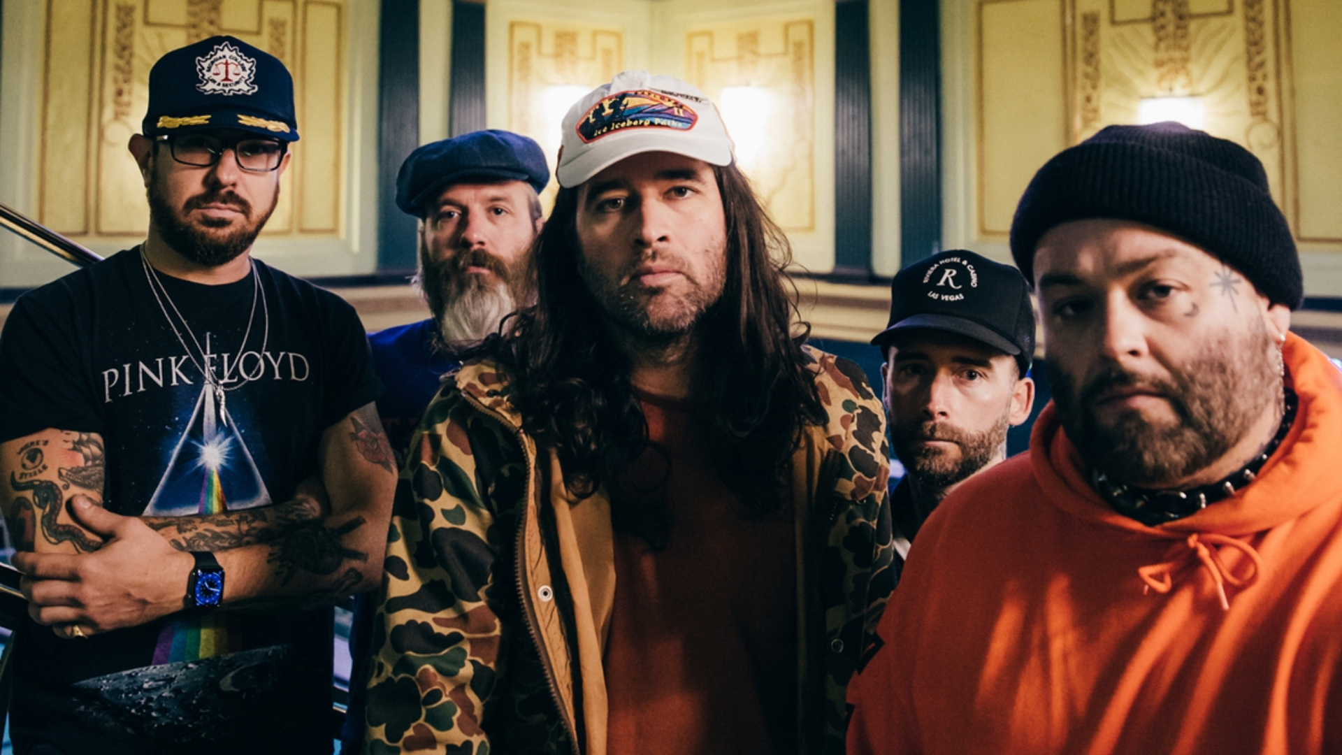 Os cinco integrantes do Alexisonfire posam juntos em fotografia promocional, usando bonés, gorros e roupas casuais, em um ambiente interno.