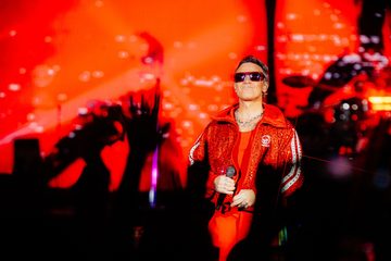 Robbie Williams usa roupa vermelha e óculos escuros enquanto segura um microfone durante show no Nubank Parque, em São Paulo.
