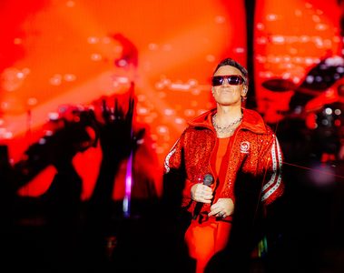 Robbie Williams usa roupa vermelha e óculos escuros enquanto segura um microfone durante show no Nubank Parque, em São Paulo.