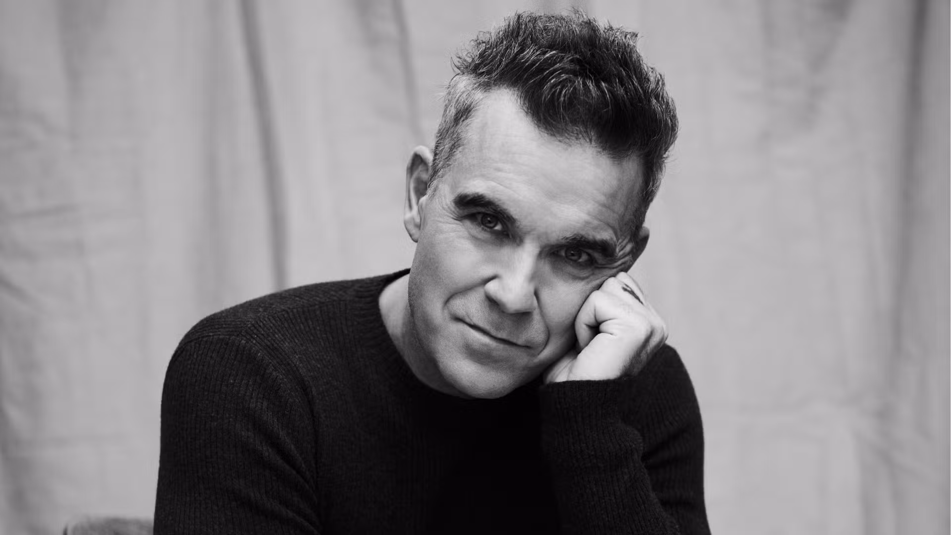 Retrato em preto e branco de Robbie Williams, que retorna ao Brasil para show em São Paulo